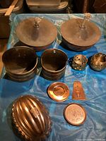 Overview photo showing entire lot of vintage brass and copper items including large torches, containers, mold, trivet, plaque, and small holders on blue tarp.