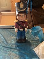 Front view of ceramic toy soldier figurine showing detailed face, blue hat with gold emblem, red jacket, blue pants, and black boots.