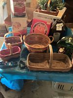 Photo showing four assorted Longaberger woven baskets on a blue surface with various holiday and decorative items in the background.