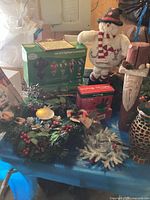 Overall view of Christmas decorations lot including knit snowman, wreaths, boxes of lights, and assorted ornaments.
