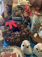 Christmas wreath, white glitter owls, and candle holder with poinsettia next to artificial greenery and elf figurine