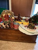 Various Christmas decorations arranged on a wooden chest including trees, wreaths, a candle, figurines, ornaments, and a tree skirt.