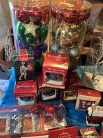 Photo showing a variety of large colorful Christmas ball ornaments along with four M.I. Hummel collectible boxed ornaments and a clear box with silver metallic reindeer decorations tied with a red ribbon.