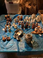 Several groups of vintage collectible salt and pepper shakers arranged on a blue tarp. Includes pairs and singles in wood, ceramic, metal, and glass with various decorative designs and shapes.