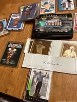 Photo showing a range of baseball and football cards on a table including a boxed Super Bowl XXXIII set and gold tone Danbury Mint cards