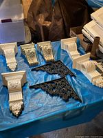 Photo showing all decorative corbels including white carved wood, grapevine design, and black metal corner brackets on blue sheet.