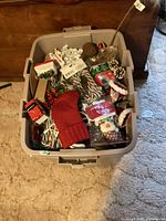Top view of plastic storage bin packed with Christmas crafting supplies including knitted stockings, candy canes, and various decorative items