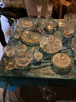 Photo showing the full assortment of crystal items arranged on a blue cloth, including candle sticks, plates, bowls, and candy dishes.