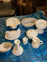 Full view of the nine milk glass pieces laid out on a blue surface showing their shapes and textures.