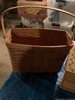 Rectangular woven natural wood basket with handle shown standing upright in a basement/storage area.