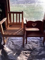 Pair of chairs side by side: natural wood slatted armchair next to smaller wooden child's chair with heart cut-out backrest and attached desk.