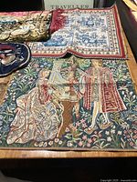 Old vintage pennants and tapestry pieces displayed on a wooden table, showing medieval-style tapestry and other fabric pieces in various colors.