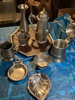 Wide view of all pewter items arranged on the tray on a blue cloth surface.