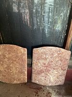 Photo showing two rectangular pink marble table tops leaning against a dark wall, highlighting the natural marble pattern and shape.