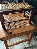 Photo showing one stool placed on top of another for size comparison and detail of woven cane seat and wooden frame.
