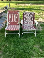 Front view of two folding lawn chairs side by side on grass, showing different geometric woven fabric patterns in red and beige with metal frames and wooden armrests.