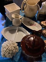 Overview of vintage items including ceramic pitchers, white divided dish, porcelain figurines, and brown glazed bean pot