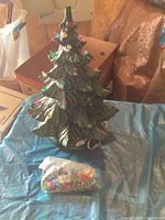 Green ceramic Christmas tree with bulbs installed and replacement bulbs bag on blue tarp.
