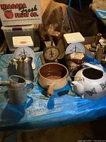 Overview of collection showing vintage scales, teapot, coffee pot, oil can, ceramic pot, and decorative tins on blue tablecloth.