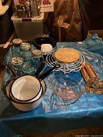 View of whole lot showing blue ball jars, enamelware pans, pink depression glass bowl, wire cake stand, magician hat vase, wooden rolling pin, and small brass decorative piece
