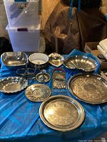 Photo showing entire lot of vintage silver items arranged on blue cloth, includes bowls, trays, candle holder, grater.