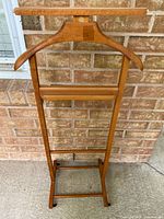 Full view of wooden valet stand showing hanger, tray, bars and casters