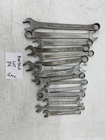 Top-down view of all 16 combination wrenches laid out in a line, sizes vary from small to large. Wrenches have open and box ends. There is a handwritten note marked 'Maxsold Lot 94, 16 pcs'.