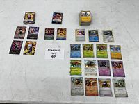 Top-down view showing three groups of collectible cards arranged on a table: Dragon Ball Z cards, a smaller stack of game cards, and a larger variety of Pokémon cards.