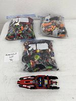 Three large ziplock bags containing assorted LEGO pieces and one partially assembled LEGO model placed outside the bags on a white surface.