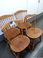 Four colonial style wooden chairs grouped together showing spindle back and contoured seats.