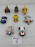 Front view of all vehicles including police car, sports car, ambulance, helicopter, jet, and beasts, arranged on a white surface with lot number card.