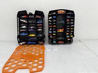 Photo showing two open black plastic carrying cases with Hot Wheels cars inside, front view.