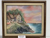 Framed oil painting showing coastal cottages near the cliffs by the ocean, under a colorful sky