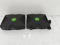 Pair of original Xbox consoles side by side showing top and front with logo and ports