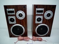 Pair of two wooden speakers with wood grain finish, each having four separate speaker drivers and wired speaker cables in front.