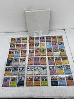 Wide image showing all 54 holographic Pokémon cards laid out flat with a white binder in the background. Cards are sleeved and organized in rows.