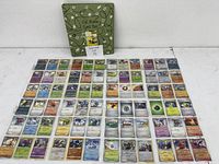 Top-down photo of 72 holographic Pokémon cards arranged neatly outside a green themed binder with decorative design and a sign showing lot number.