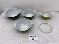 Four green and white Pyrex mixing bowls of varying sizes with one clear glass lid included.