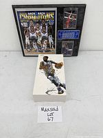 Lot arranged on white surface showing both sealed figure box and framed plaque with MaxSold lot tag