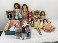 Lot overview showing all twelve vintage dolls arranged on white surface, some boxed, others loose.