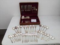 Vintage silverware displayed including large serving spoon, forks, spoons, and knives with wooden case.