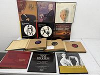 Vintage vinyl records and album covers displayed on a white surface showing classical composers and swing era titles, with paper sleeves and printed materials