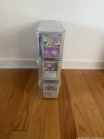 Front view of three stacked clear plastic card storage boxes each with a single Pokemon card displayed in front.