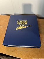 Closed blue binder labeled 'Card Collector's Ultimate' placed on wooden surface.