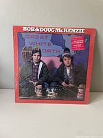 Front view of the sealed album cover with red background showing Bob and Doug McKenzie sitting at a table.