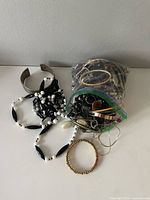 Bag of assorted costume jewelry pieces including a silver-tone cuff bracelet, various beaded bracelets and necklaces in black, white, and gold colors.