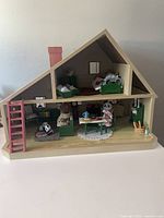 Front view of furnished Calico Critters wooden dollhouse with animal figures in living and bedroom areas.