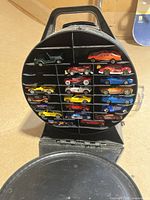 Front open view showing 25 die-cast toy cars arranged in rows in circular slots inside the open carrying case.