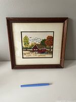 Full view of the framed crewel embroidered artwork depicting a covered bridge and trees.