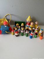 Wide view of the entire collection including the blue pull-along train with a red figure, multiple wooden figurines in colors red, green, blue, yellow, and a yellow conical-hat figure.